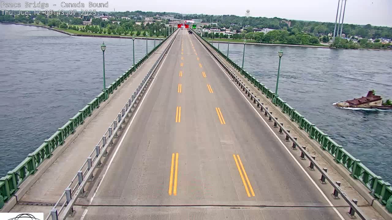 A long bridge spans a body of water on a partly sunny day, with a few vehicles visible on the roadway.