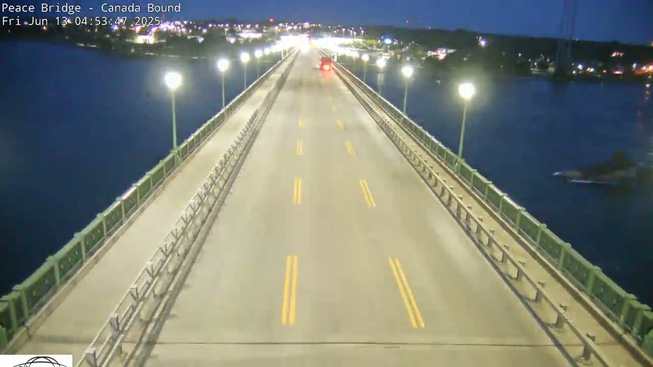 A single vehicle drives on a bridge at night over dark water, lit by streetlights.