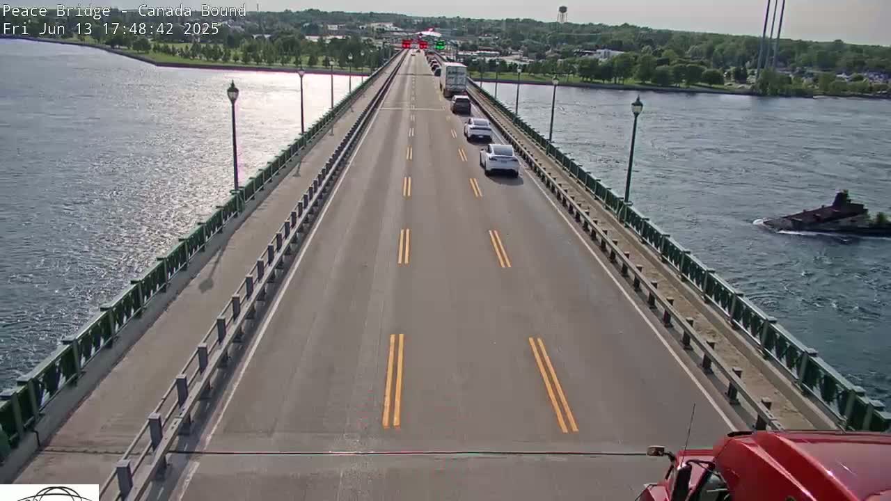 A bridge over water with several cars and a truck driving on it, under a sunny sky.