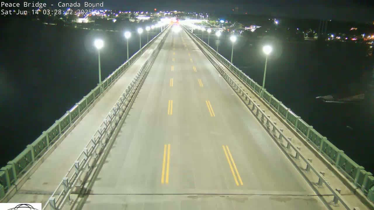 A mostly empty highway stretches across a bridge at night, illuminated by lights along the sides, over dark water.