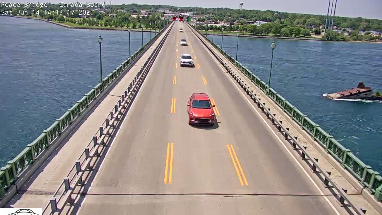 Several cars drive across a bridge over a body of water on a sunny day.