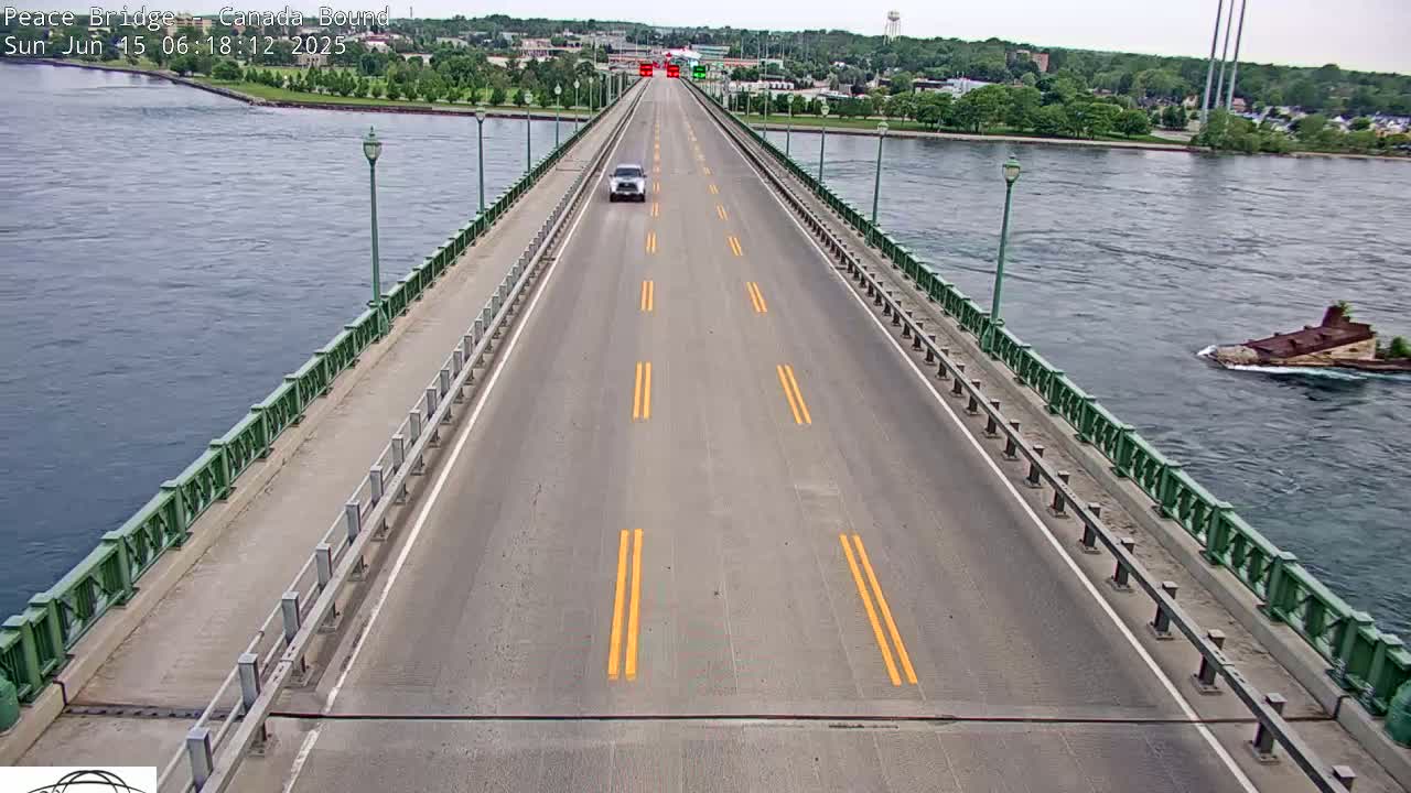 A single vehicle drives on a bridge over a body of water on a partly cloudy day.