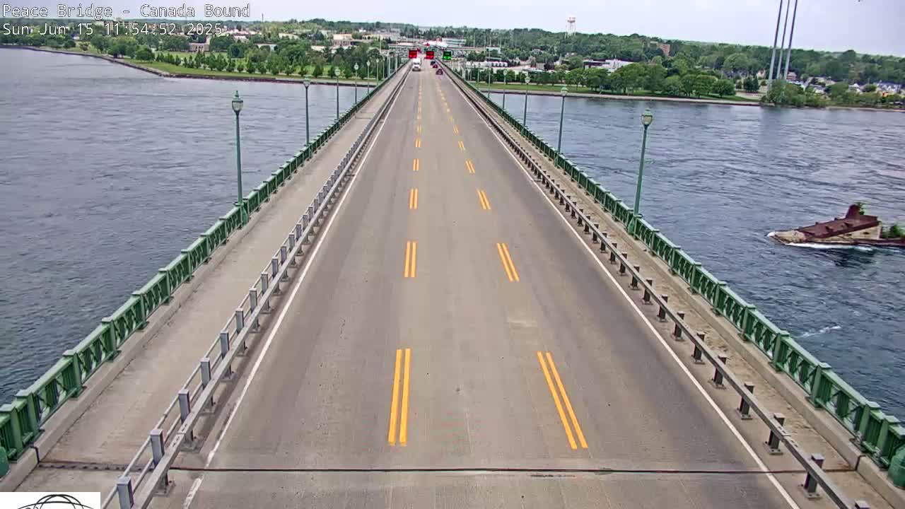 A bridge with a few cars driving on it stretches across a body of water on a partly sunny day.