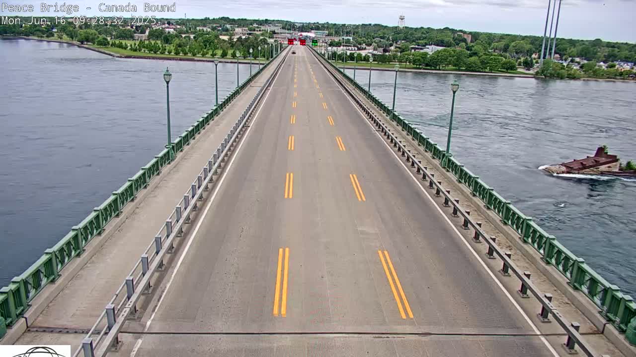 A long bridge roadway with yellow lane markings stretches across a body of water under partly cloudy skies, with a small vessel visible in the water to the right.