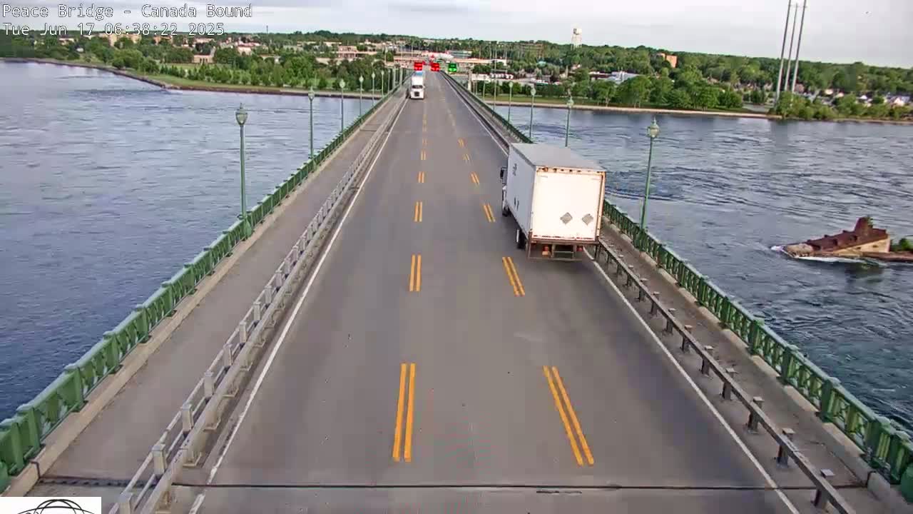 A bridge roadway with two trucks and a partially submerged vessel in the water below on an overcast day.