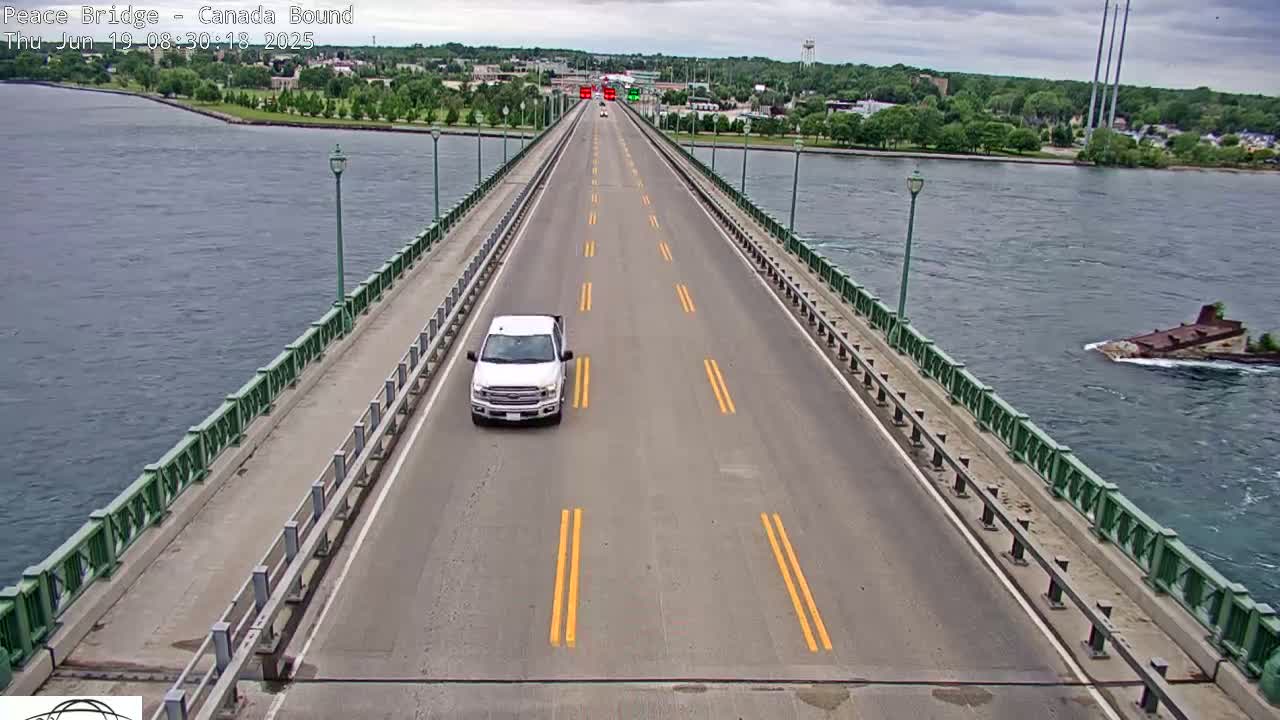 A white pickup truck drives across a bridge over water under partly cloudy skies.