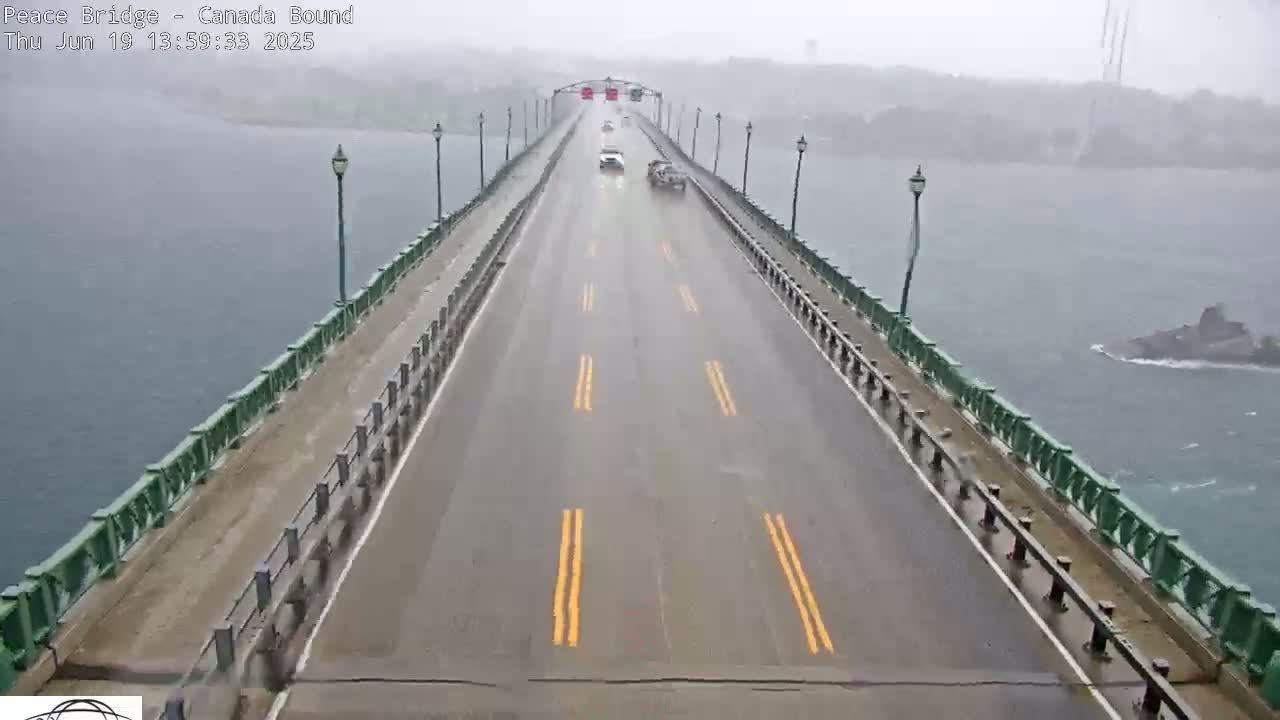 A wet, two-lane bridge stretches across a body of water under a hazy sky, with a few vehicles visible on the road.