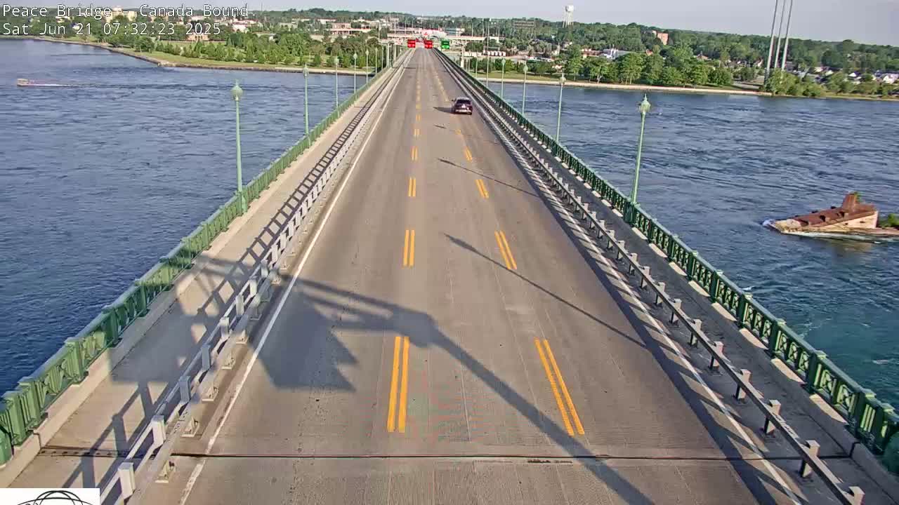 A sunny, overhead view of a two-lane bridge over a body of water, with one car visible on the road.