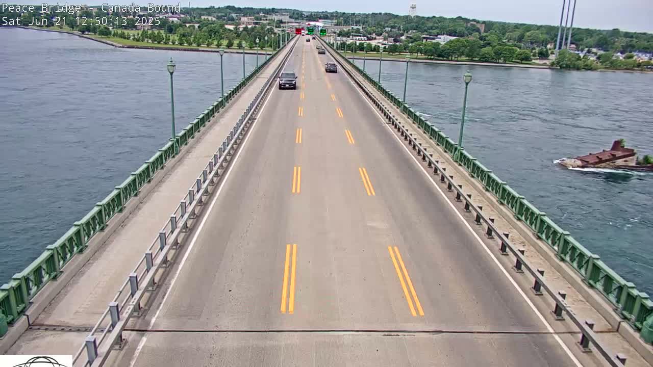 A bridge road with several cars driving on it overlooks a calm body of water on a sunny day.