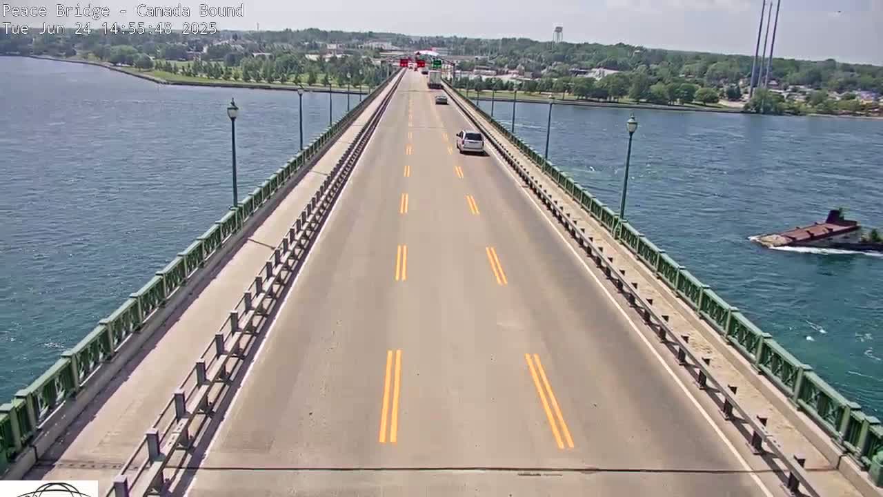 A bridge roadway with a few vehicles, bordered by railings, stretches across a body of water on a sunny day.