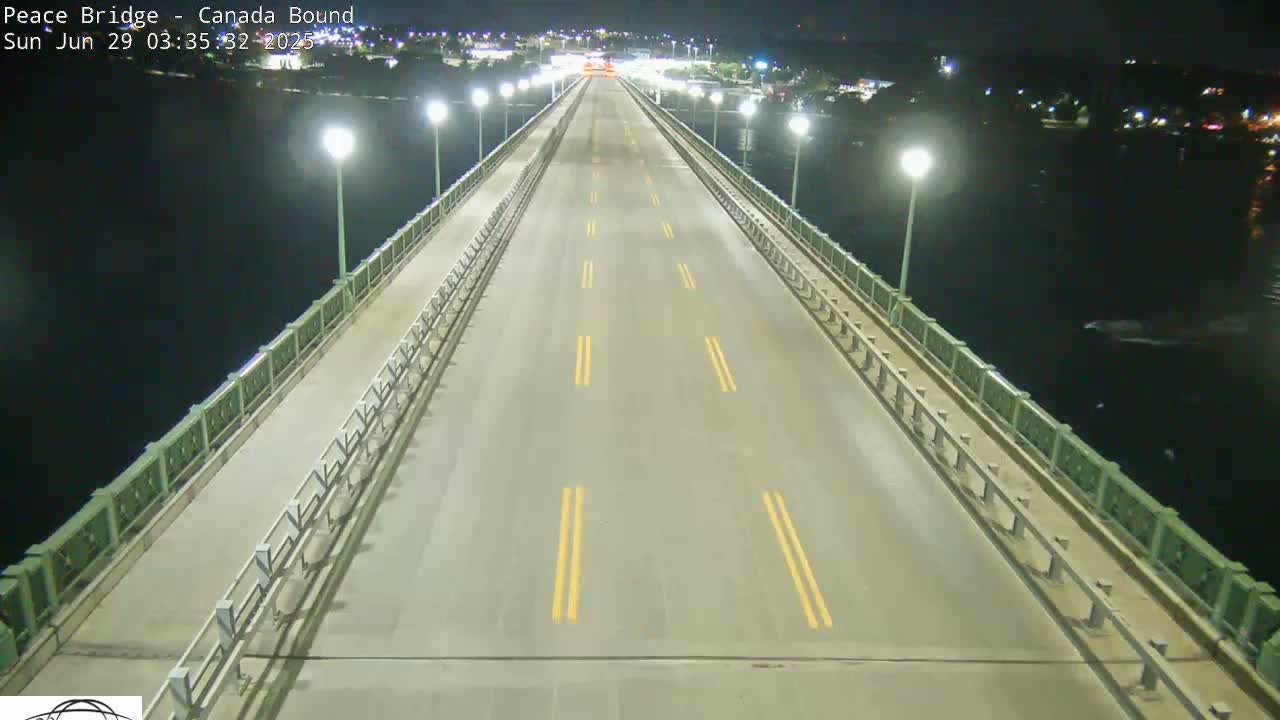 A mostly empty bridge at night, lit by streetlights, stretches across dark water.