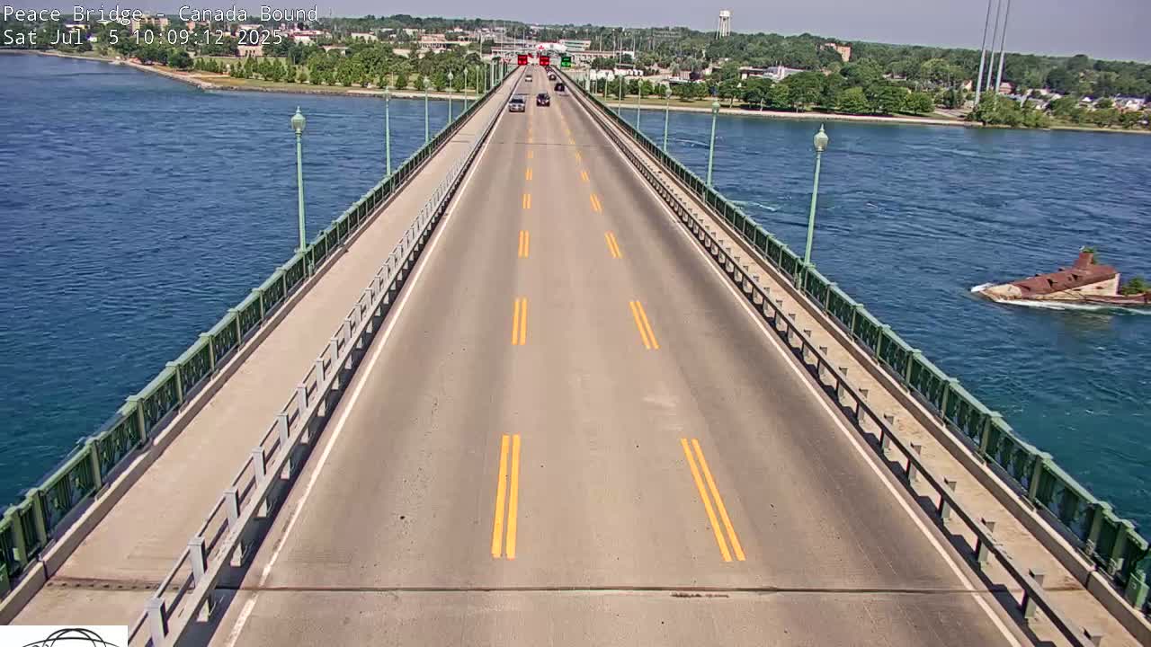 A long bridge roadway with several cars driving on a sunny day stretches across a body of water with a small island visible in the distance.