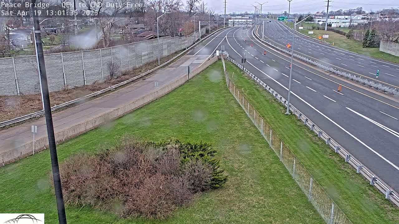A slightly overcast view of a multi-lane highway with sparse traffic, bordered by grassy areas and fences.