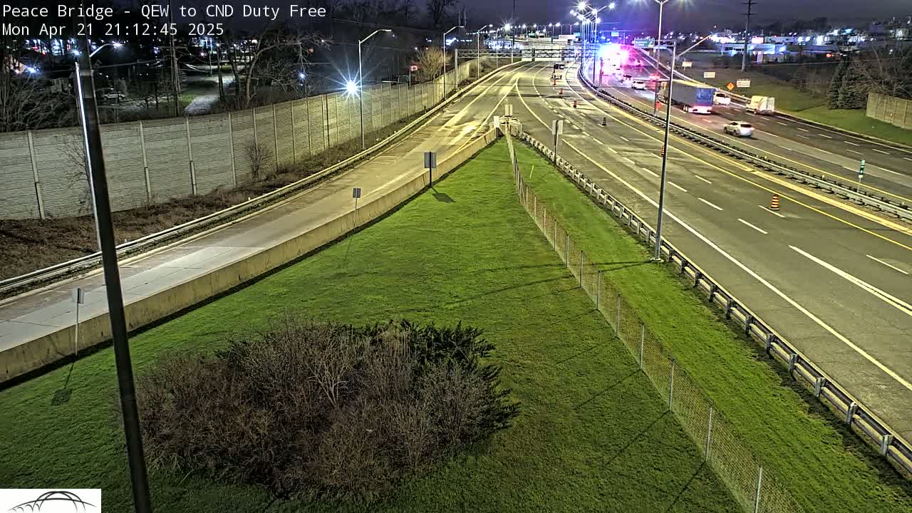 A nighttime aerial view of a highway interchange with several vehicles driving on it, bordered by grassy areas and fences.