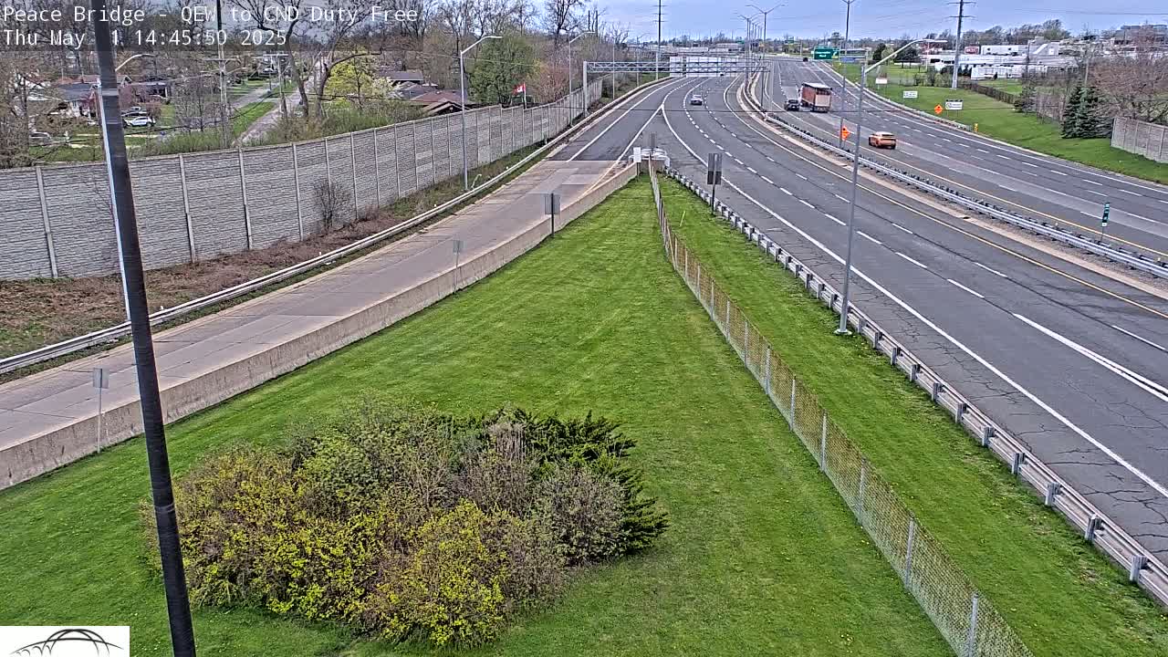 A grassy area next to a multi-lane highway on a partly cloudy day with a few vehicles visible.