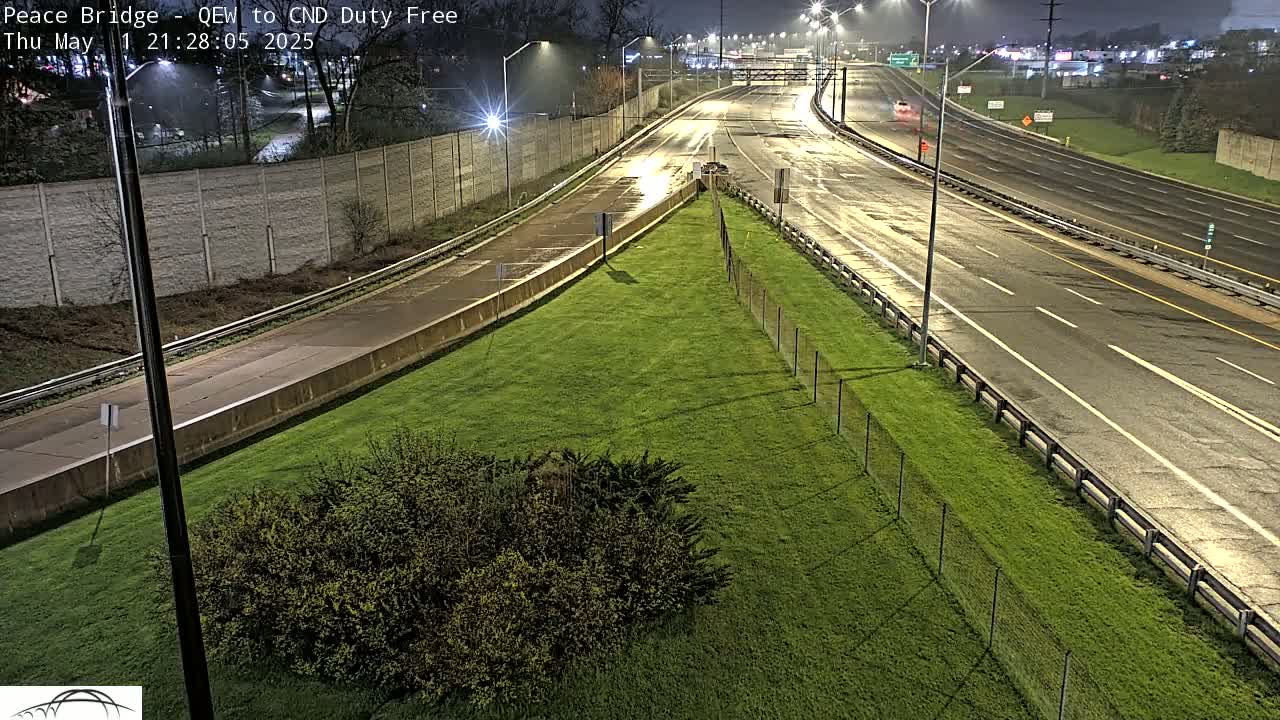 A wet highway at night, bordered by grassy areas and a chain-link fence.