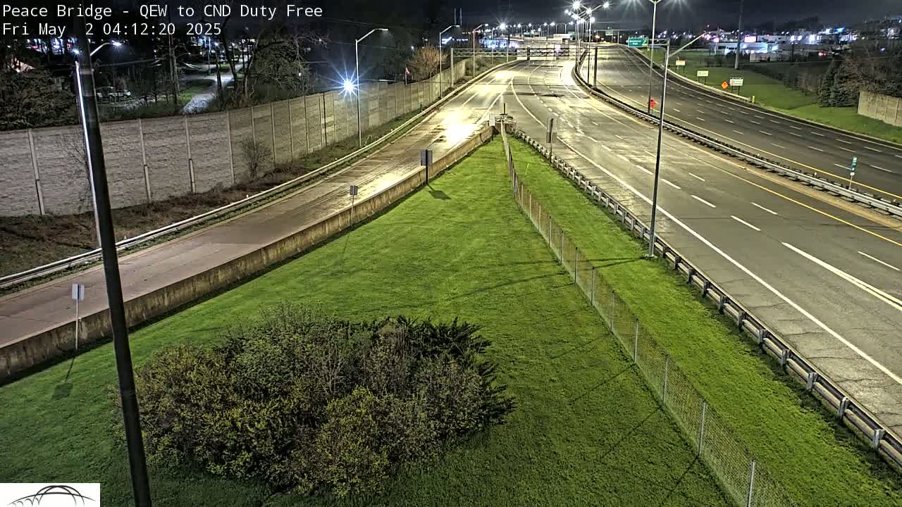 A grassy area beside a multi-lane highway at night, illuminated by streetlights, with a few vehicles visible in the distance.