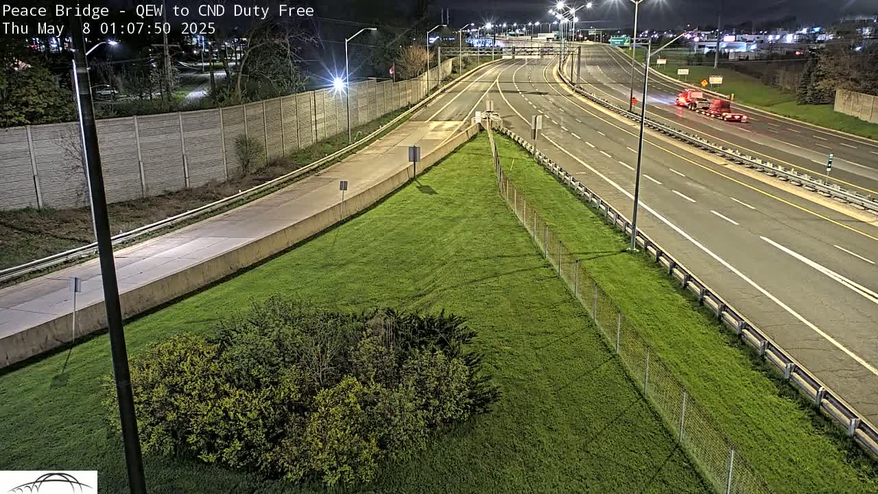 A nighttime, overhead view of a multi-lane highway with a few vehicles and grassy areas alongside.