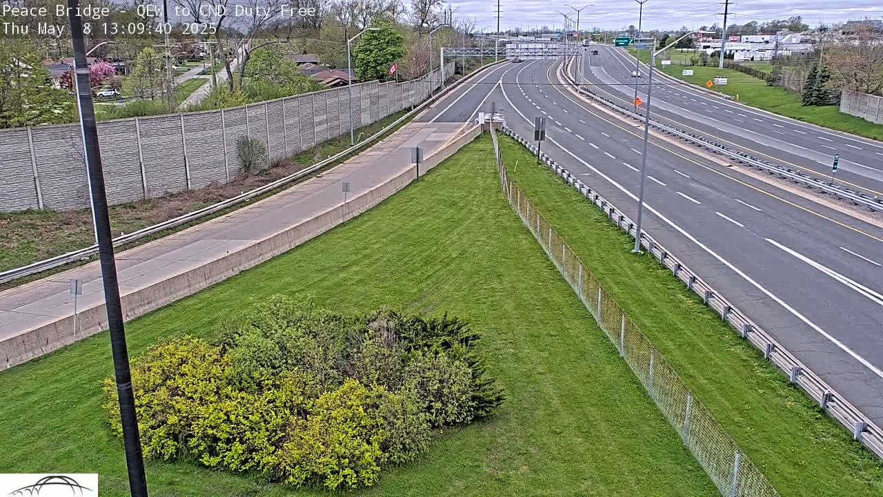 A grassy area with some shrubs borders a multi-lane highway on a partly cloudy day.