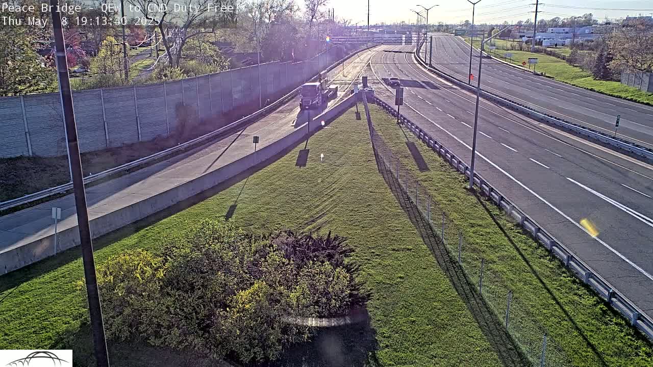 A sunny day reveals a highway scene with a few vehicles, grassy areas, and a concrete barrier separating lanes of traffic.