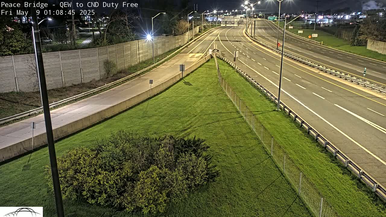 A nighttime, high-angle view of a multi-lane highway bordered by grassy areas and chain-link fences.