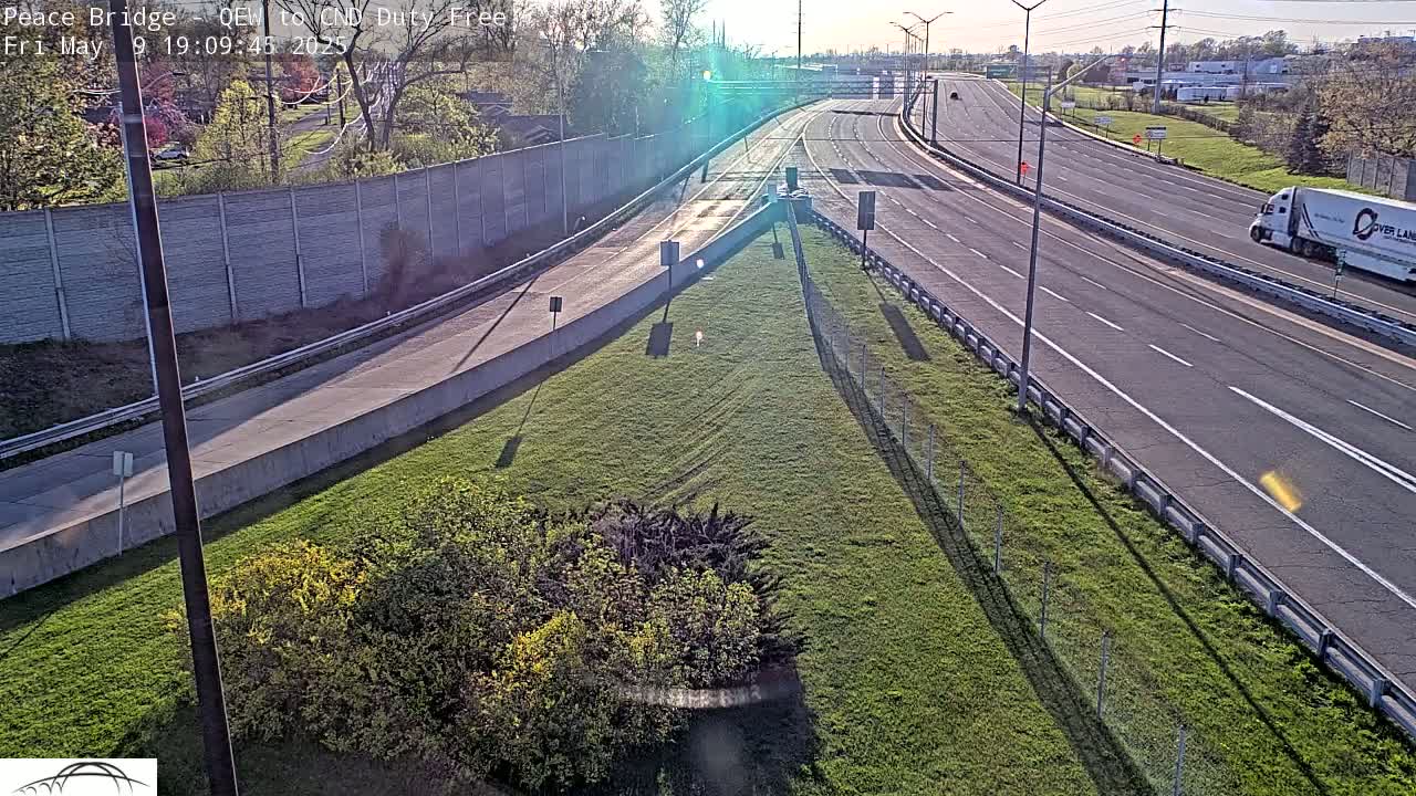 A high-angle view shows a highway interchange on a sunny day with some light traffic and grassy areas between roadways.
