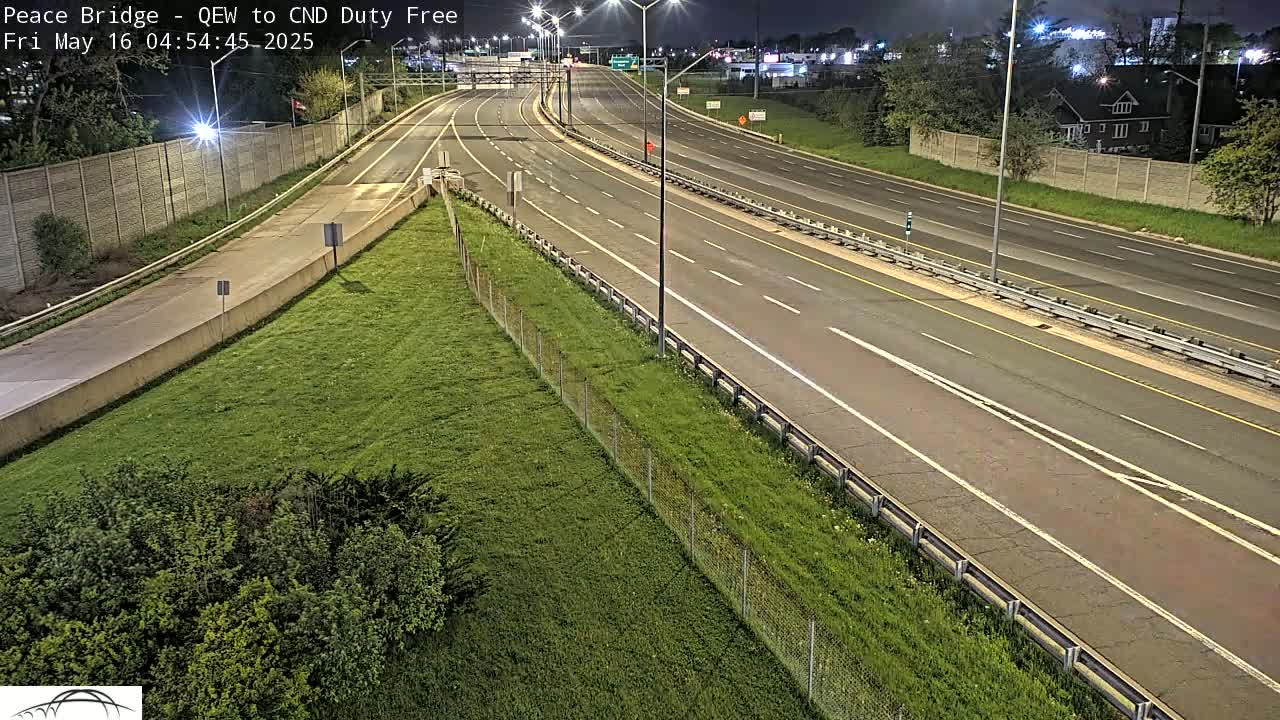 A mostly empty highway at night, bordered by grassy areas and fences, under nighttime lighting conditions.