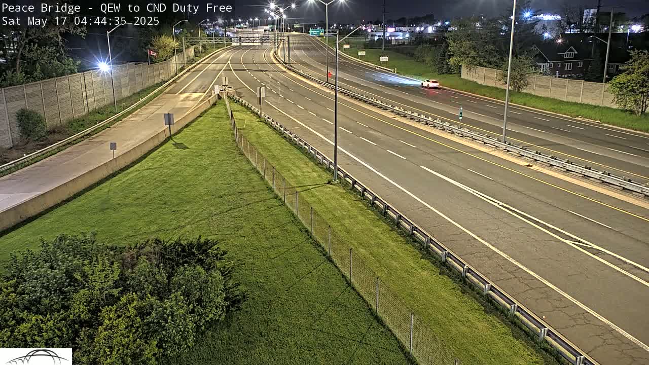 A mostly empty highway curves through a grassy area at night under artificial lights.