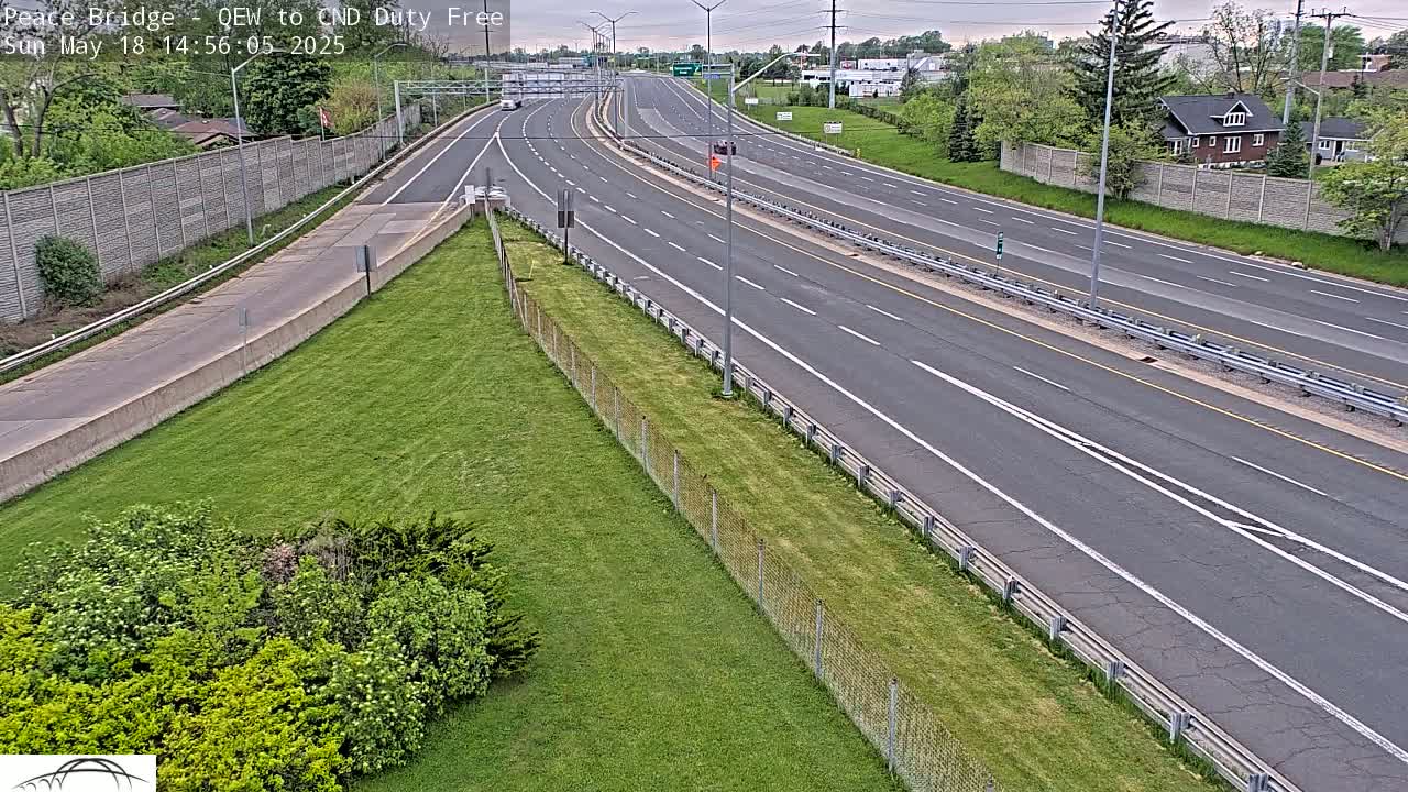 A mostly empty highway with grassy areas and a chain-link fence on either side on an overcast day.