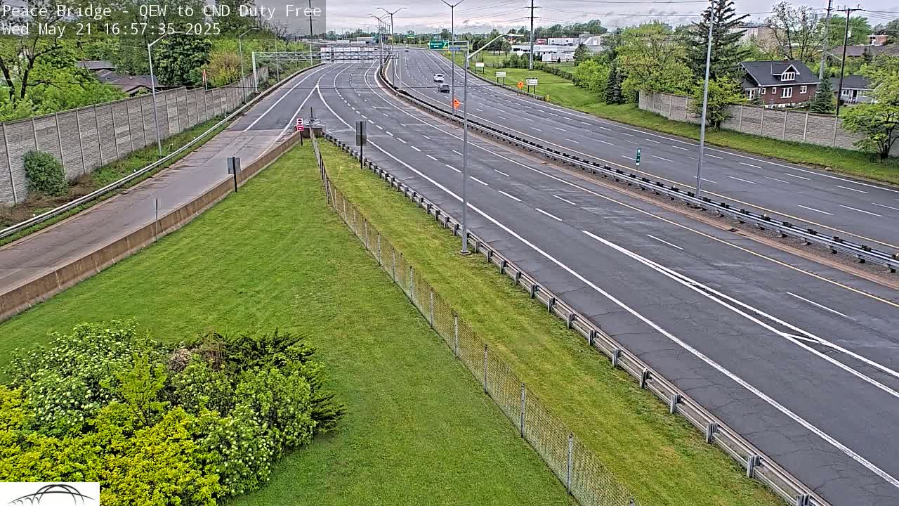 A mostly empty highway with a grassy median and trees visible in the background on an overcast day.