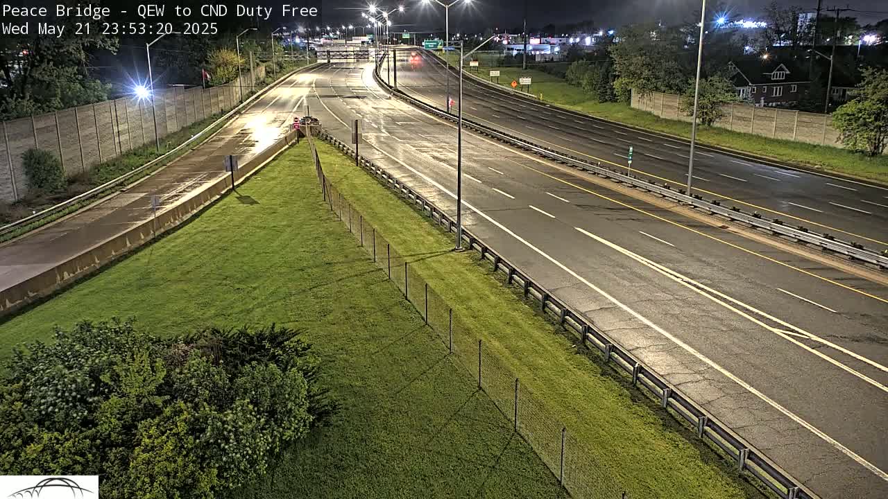 A nighttime, wet highway scene shows a multi-lane roadway curving gently to the left, with sparse traffic and grassy areas alongside.