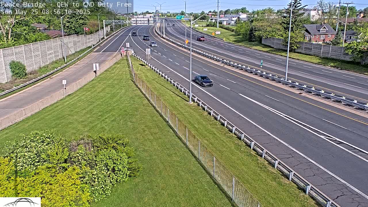A multi-lane highway with several cars traveling on a sunny day, bordered by grassy areas and a chain-link fence.