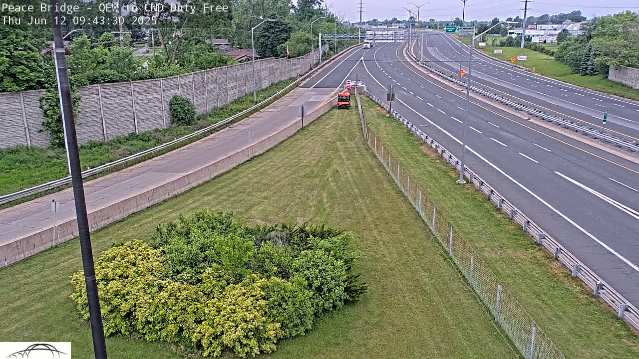 A mostly empty highway with a small orange vehicle on a grassy area beside it under an overcast sky.