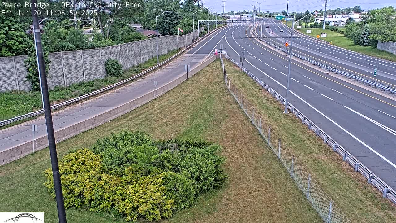 A multi-lane highway stretches into the distance under a partly cloudy sky, bordered by grassy areas and chain-link fencing.