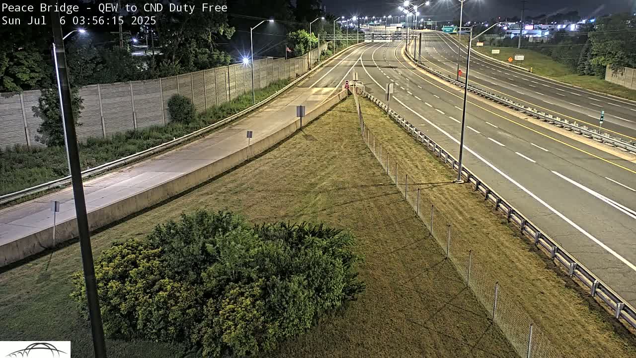 A nighttime view of a highway interchange with sparsely traveled lanes and a grassy median, illuminated by streetlights.
