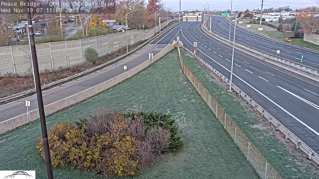 A nighttime high-angle view shows a multi-lane highway with sparse traffic, bordered by a chain-link fence and dry, brown grass.