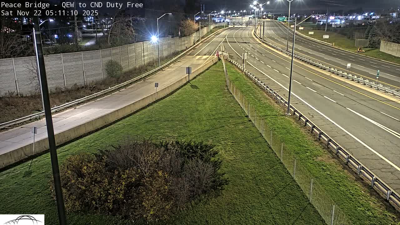 An elevated view captures a multi-lane highway interchange with concrete barriers and a grassy median, brightly illuminated by streetlights under a clear, dark sky during nighttime or very early morning.