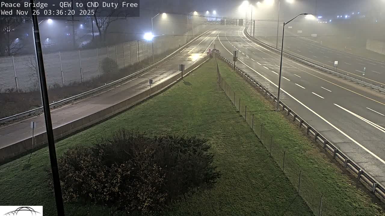 An empty, multi-lane highway system curves through the frame at night, its wet asphalt gleaming under the diffused light of numerous streetlights through a heavy fog.
