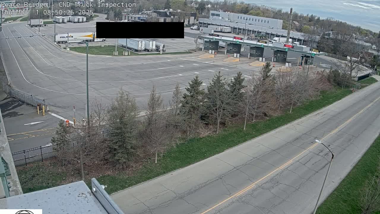 An overhead view of a truck inspection station with several trucks parked nearby, on a partly cloudy day.