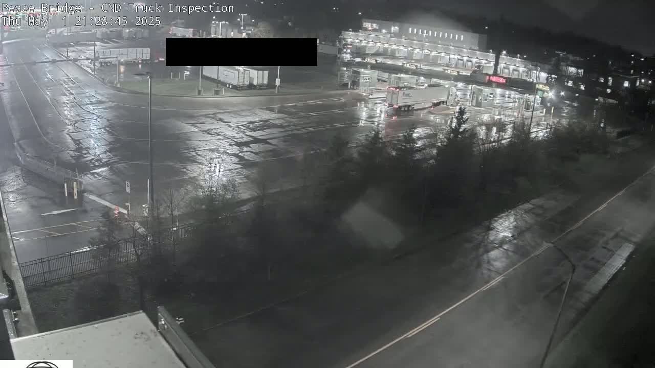 A wet, nighttime view of a truck inspection station with several semi-trucks and buildings.