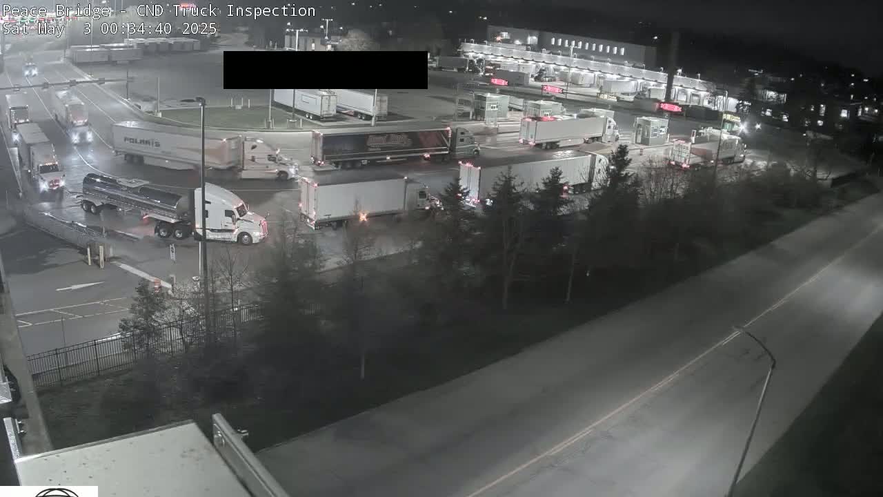 A nighttime, aerial view of a truck inspection area shows numerous semi-trucks and tankers parked and driving around the facility.