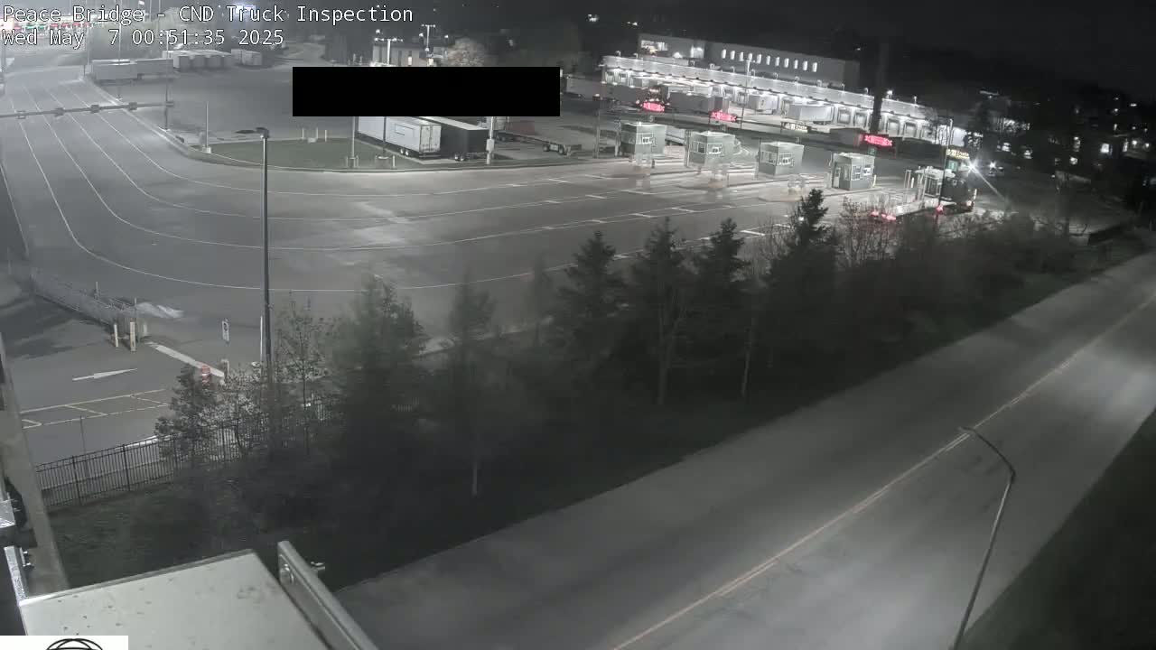 A nighttime overhead view shows a truck inspection station with several trucks and cars, surrounded by trees and roads.