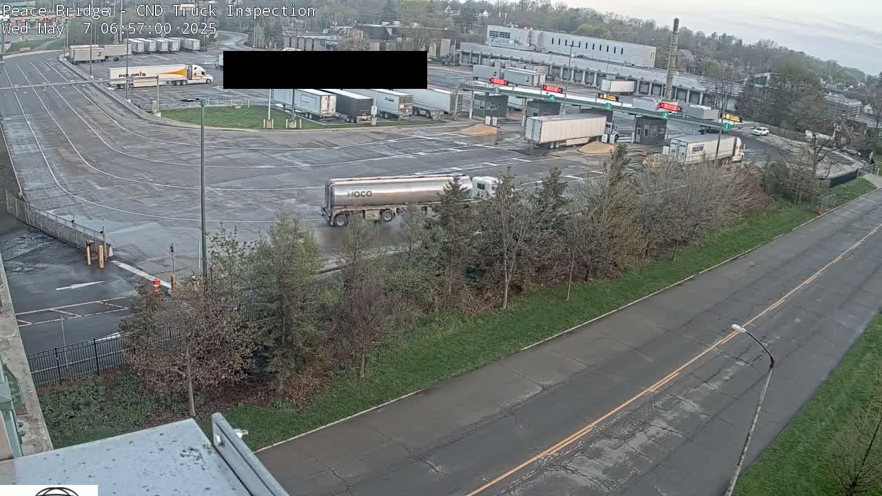 A large truck inspection station with several semi-trucks parked and moving around on a wet, overcast day.
