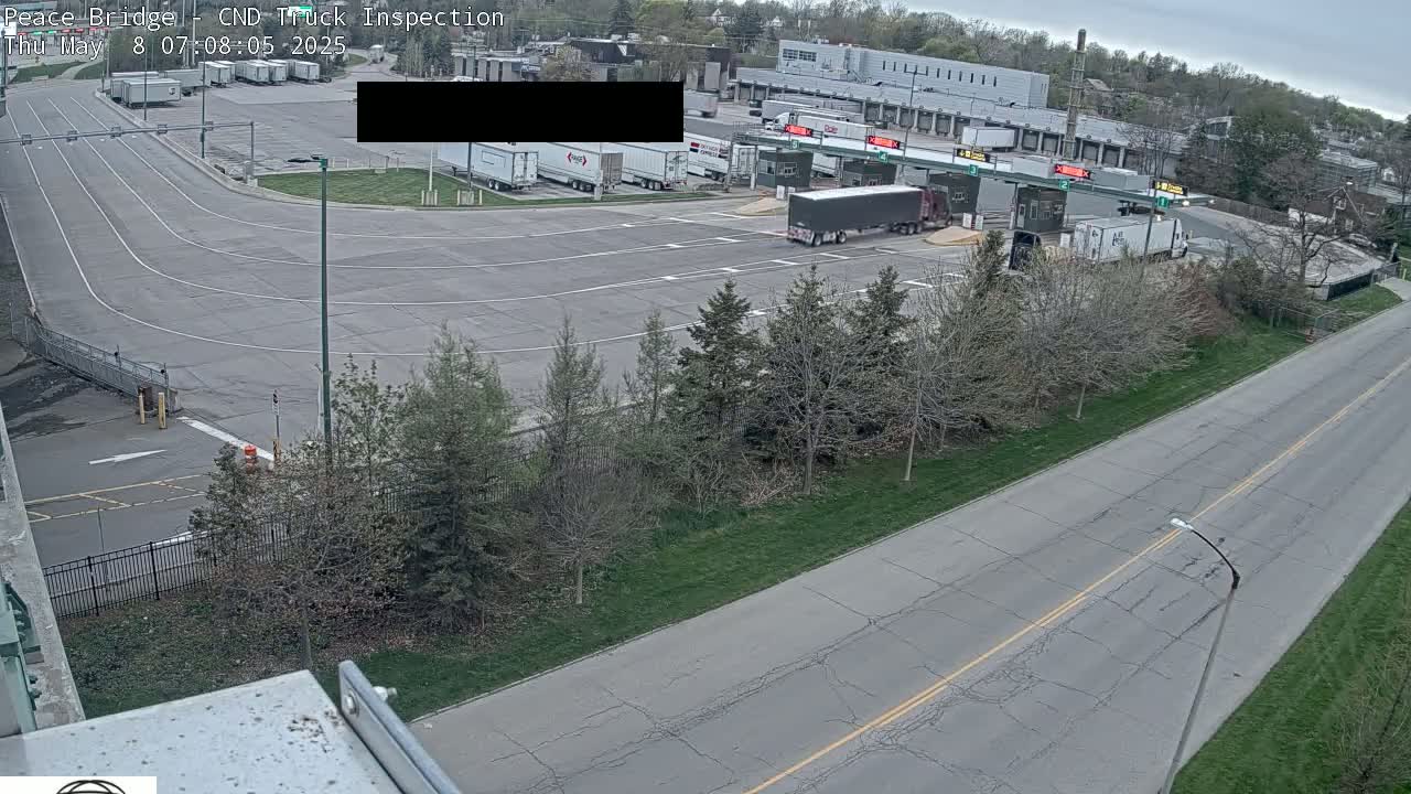 An overhead view shows a truck inspection station with several semi-trucks, surrounded by trees and a road under an overcast sky.