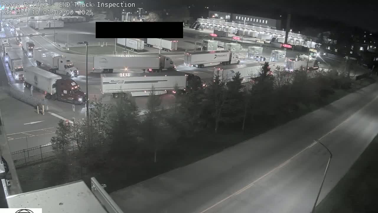 At night, numerous semi-trucks are parked and moving around a truck inspection area.
