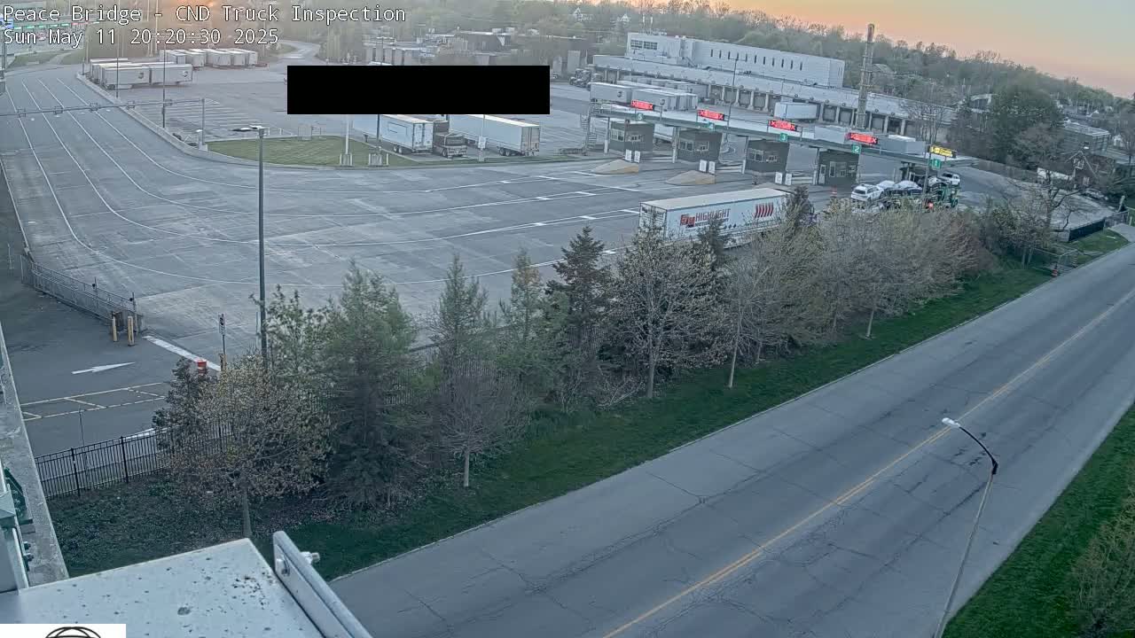An aerial view shows a truck inspection station with several semi-trucks, cars, and a road under a twilight sky.