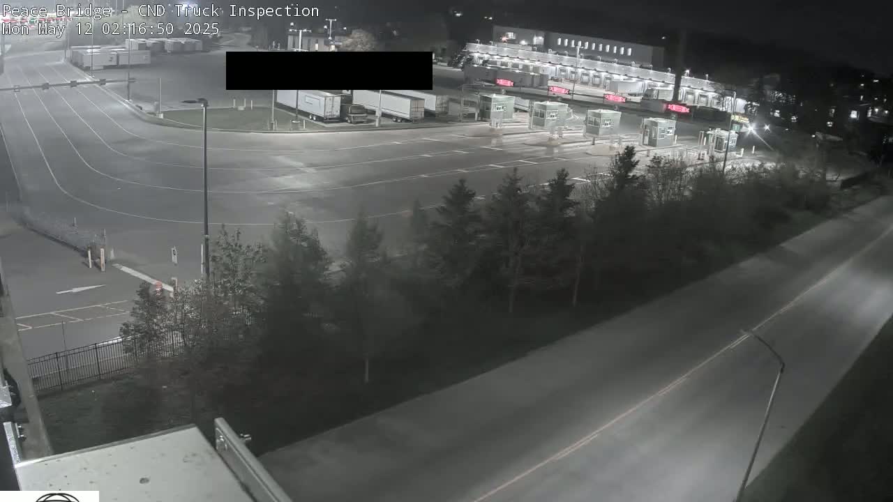 At night, a truck inspection area with several trucks and inspection booths is shown, alongside a roadway with sparse vegetation.