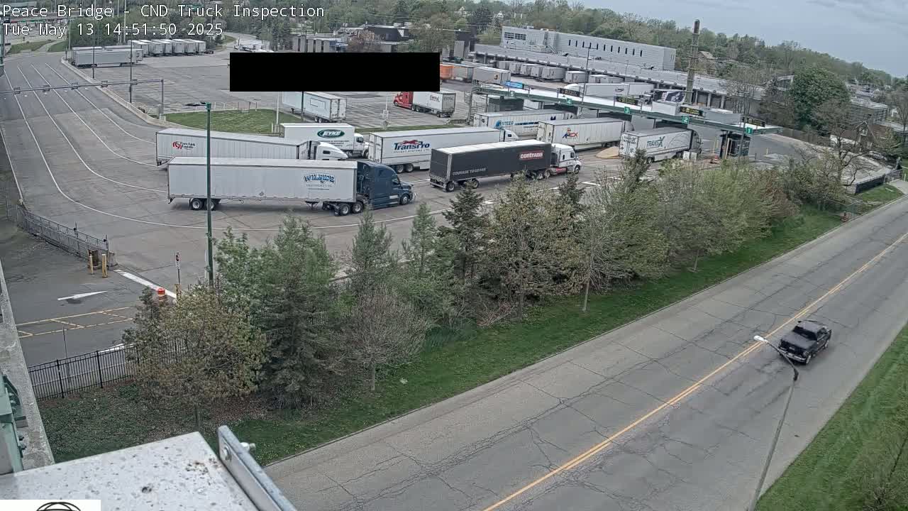 Several semi-trucks are parked in a truck inspection area on an overcast day.