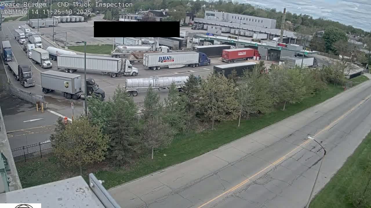 A truck inspection area with numerous semi-trailer trucks maneuvering in a paved lot on a partly cloudy day.