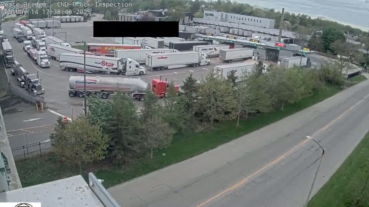 Numerous semi-trucks are parked and moving around a truck inspection area on an overcast day.